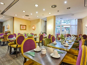 Frühstücksraum.jpg Frühstücksrestaurant mit gedeckten zweier Tischen und lila-gelben StühlenBreakfast restaurant with two set tables and purple and yellow chairs