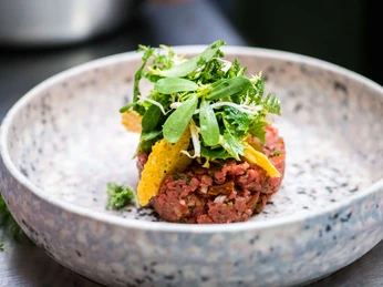 Frisch zubereitete Speise im Haus Stemberg Eine edle Vorspeise aus rohem Fleisch, dekoriert mit frischen Kräutern und knusprigen Chips.