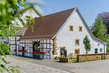 Fachwerkhaus mit weißen Wänden und braunen Details in einer gepflegten Umgebung unter blauem Himmel.