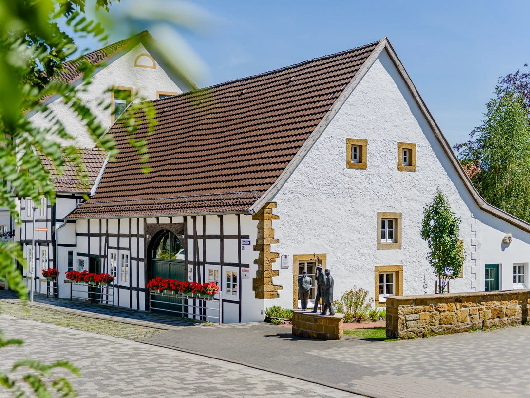 Fachwerkhaus mit weißen Wänden und braunen Details in einer gepflegten Umgebung unter blauem Himmel.