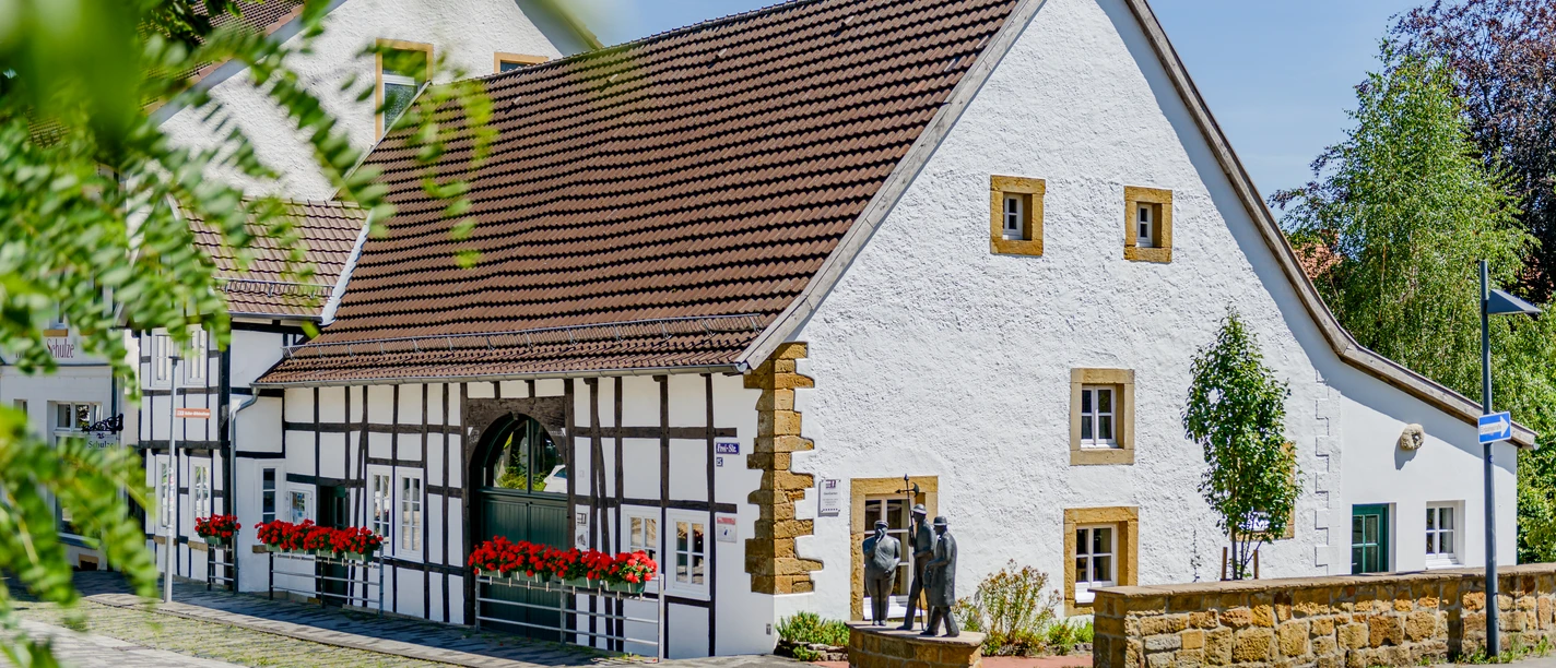 Fachwerkhaus mit weißen Wänden und braunen Details in einer gepflegten Umgebung unter blauem Himmel.