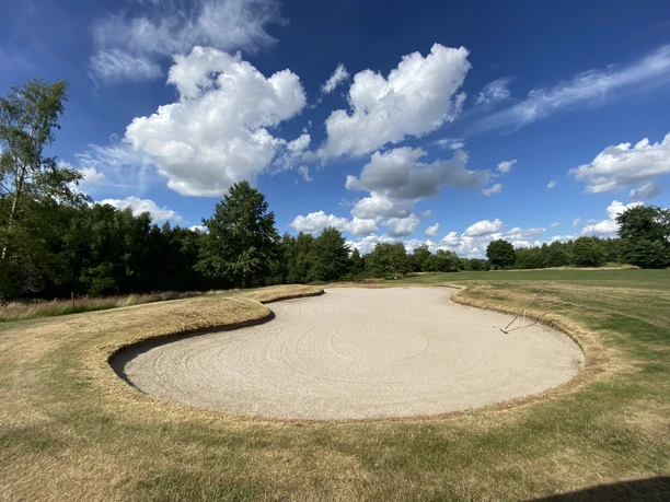 Blauer Fasan Golf 4.jpg Harmonisch geschwungener Sandbunker auf grünem Golfplatz unter blauem Himmel mit weißen Wolken.