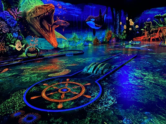 Schwarzlichtgolf.jpeg Faszinierendes Schwarzlicht-Minigolf mit lebhaften Unterwasserszenen und leuchtenden Farben.