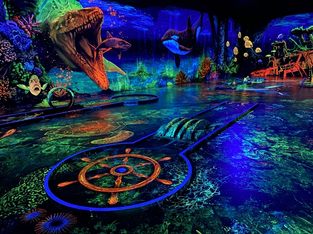 Schwarzlichtgolf.jpeg Faszinierendes Schwarzlicht-Minigolf mit lebhaften Unterwasserszenen und leuchtenden Farben.
