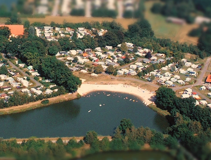 Luftaufnahme eines großen, von Wald umgebenen Campingplatzes mit Wohnwagen und Zelten an einem See.