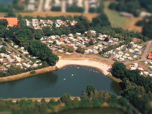 Luftaufnahme.jpg Luftaufnahme eines großen, von Wald umgebenen Campingplatzes mit Wohnwagen und Zelten an einem See.
