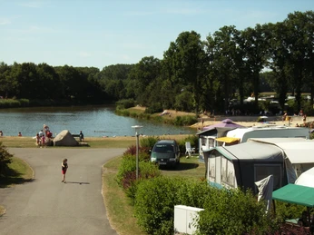 Strandblick vom Platz .JPG Campingplatz am See mit Wohnwagen, Badegästen am Sandstrand und bewaldeter Umgebung im Sommer.