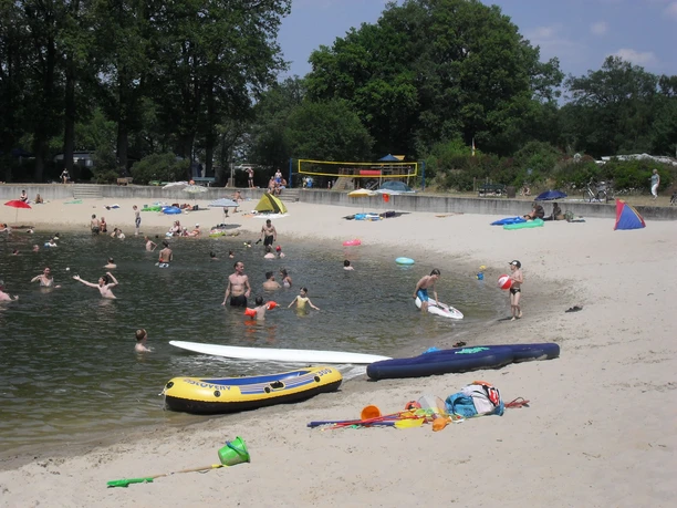Campingpark Sonnensee Strand Menschen genießen einen Sommertag am Seeufer; einige schwimmen, andere entspannen sich am Sandstrand.
