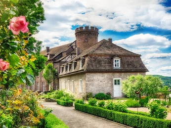 Sommer auf der Burg Herstelle Eine historische Burg mit Turm, umgeben von gepflegten Gärten und blühenden Rosen im Sommer.