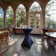 Wintergarten der Burg Herstelle mit großen Glasfenstern, eleganten Rattanstühlen und Tischen.