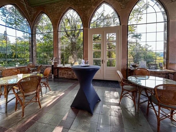 Wintergarten der Burg Herstelle Wintergarten der Burg Herstelle mit großen Glasfenstern, eleganten Rattanstühlen und Tischen.