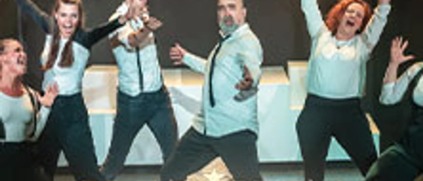 Eine fröhliche Gruppe von Künstler*innen auf der Bühne in prunkvollen Kostümen bei einer Musicalprobe.