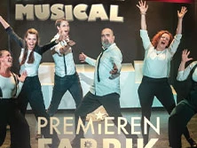 Eine fröhliche Gruppe von Künstler*innen auf der Bühne in prunkvollen Kostümen bei einer Musicalprobe.