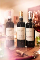 La piccola Enoteca Drei Weinflaschen von Stroppiana auf einem Tisch, daneben ein halb gefülltes Weinglas.