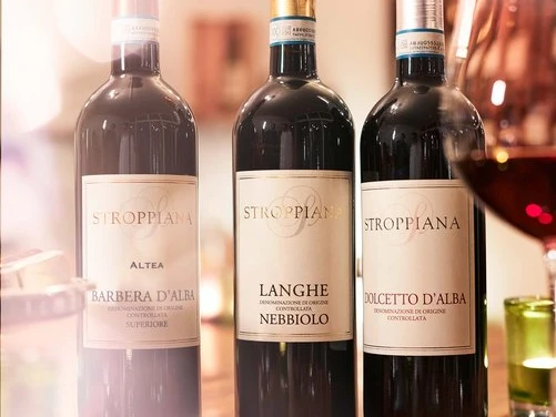 La piccola Enoteca Drei Weinflaschen von Stroppiana auf einem Tisch, daneben ein halb gefülltes Weinglas.