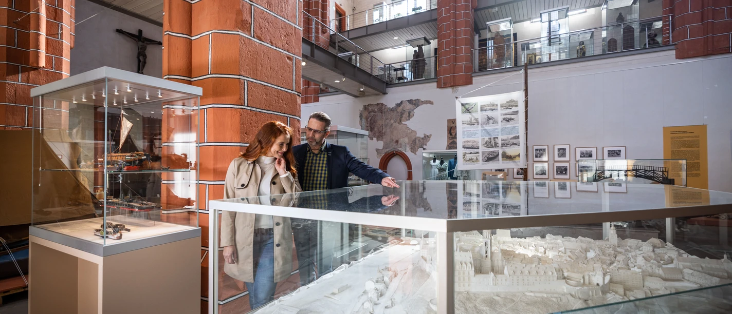 A couple looks at a detailed model in a light-flooded museum with high ceilings.