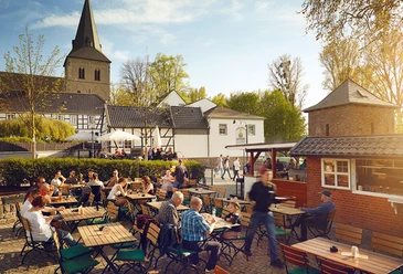 Zollhäuschen Biergarten zur Altstadt Der Biergarten mit Holztischen bietet Sitzplätze im Freien und liegt malerisch vor einer Kirche.