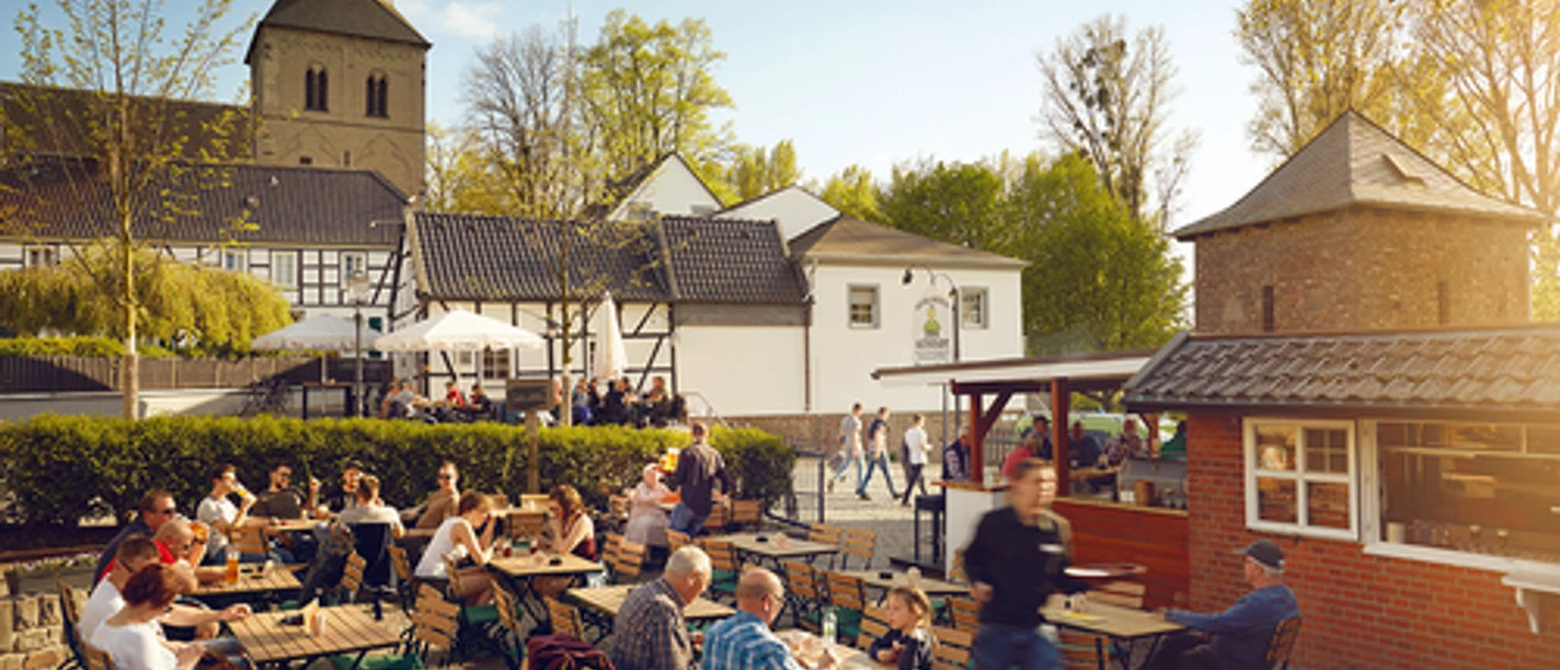 Zollhäuschen Biergarten zur Altstadt Der Biergarten mit Holztischen bietet Sitzplätze im Freien und liegt malerisch vor einer Kirche.