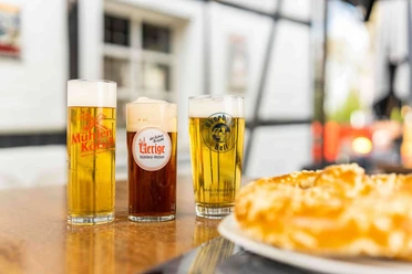 Zollhäuschen Kneipe Drei köstliche, frisch gezapfte Biere in unterschiedlich hohen, schlanken Gläsern vor Fachwerkhaus.