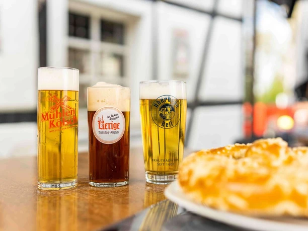 Zollhäuschen Kneipe Drei köstliche, frisch gezapfte Biere in unterschiedlich hohen, schlanken Gläsern vor Fachwerkhaus.