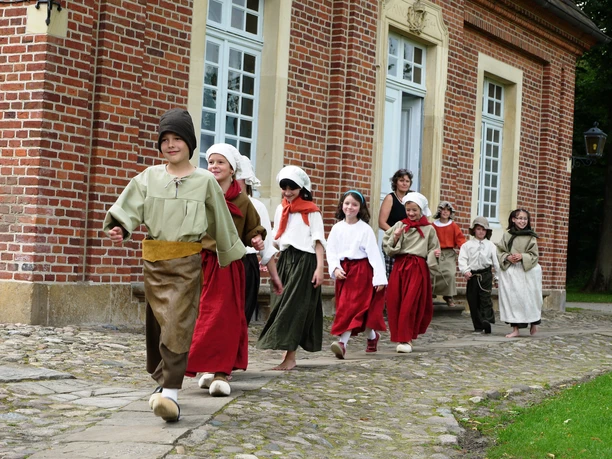 Kinder c @ Emslandmuseum Schloss Clemenswerth.JPG Kinder in historischen Kostümen gehen lachend vor dem Backsteingebäude des Emslandmuseums Clemenswerth.