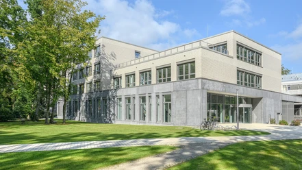 Das Reha-Zentrum am Meer ist ein modernes Gebäude mit hellem Backstein und großen Fenstern, umgeben von Grünflächen und Bäumen. Fahrräder stehen vor dem Eingang, was eine einladende und ruhige Atmosphäre schafft.