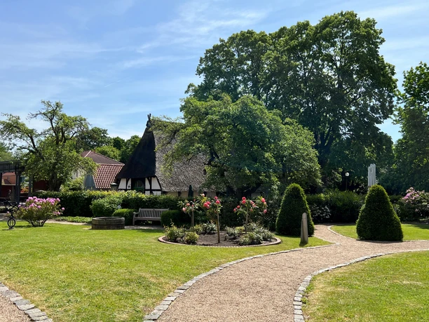 Spargelmuseum Nienburg Thatched-roof building in the middle of a green garden with surrounding, well-tended flower beds and paths.