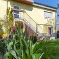 Eingang Hinterhofgarten mit blühenden Tulpen im Vordergrund vor einem gelben Haus mit Außentreppe.