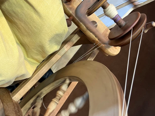 Eine Hand spinnt Garn auf einem traditionellen hölzernen Spinnrad in Bewegung.