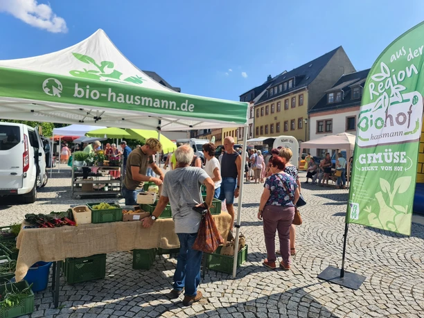 Stände mit Besuchern auf dem Regionalmarkt Geithain Das Bild zeigt einen gut besuchten Stand mit regionalen Bioprodukten am Tag. Die zahlreichen Marktstände, platzieren sich rund um den Marktplatz in Geithain.