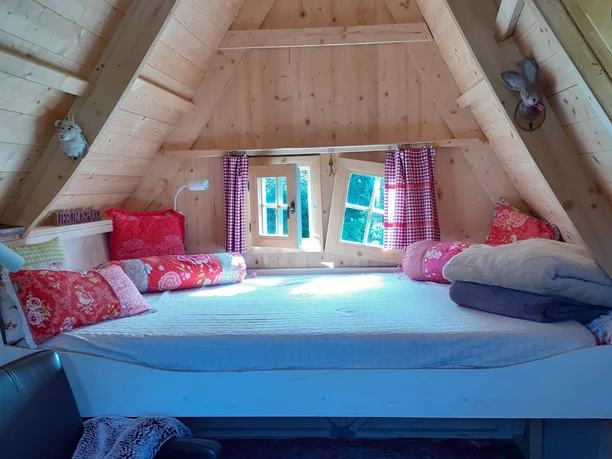 Helle Holzhütte mit einem großzügigen Dachboden-Schlafbereich, gemütlicher Dekoration und Fenstern.