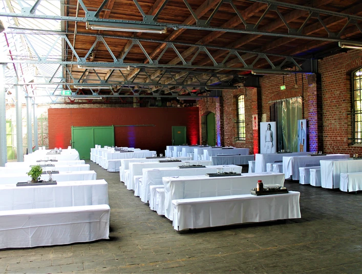 Ein großzügiger Veranstaltungsraum im alten Güterbahnhof mit weißen Tisch- und Bankbezügen.