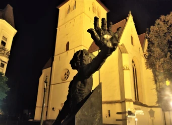 Herford-Schauergeschichten-quer -Pro-Herford-GmbH.jpg Eine imposante Skulptur vor einer beleuchteten, gotischen Kirche bei Nacht, Herford.