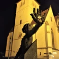 Herford-Schauergeschichten-quer -Pro-Herford-GmbH.jpg Eine imposante Skulptur vor einer beleuchteten, gotischen Kirche bei Nacht, Herford.