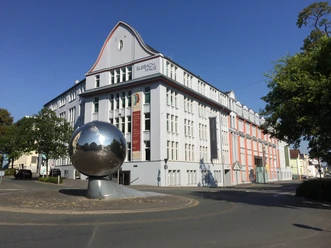 Historisches Gebäude in Herford mit markanter Fassade und großer spiegelnder Kugelskulptur davor.