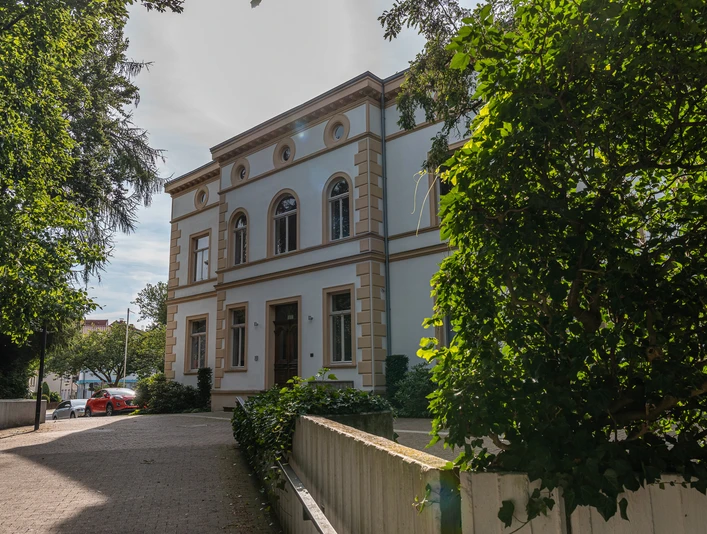 Pro_Herford_Bilder Herford_2021_109.jpg Klassizistisches Gebäude umgeben von grünen Bäumen, gepflasterter Weg führt zur hölzernen Eingangstür.