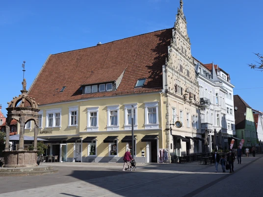 Historisches Rathaus mit markantem Giebel und umliegenden Cafés, strahlend unter blauem Himmel.