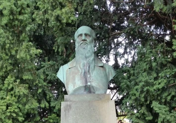 Büste von Friedrich Ludwig Jahn auf einem Sockel, umgeben von dichten, grünen Nadelbäumen.
