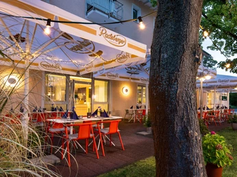 Außengastronomie im Kristallhotel FETTEHENNE Außengastronomie des Kristallhotels FETTEHENNE in Leverkusen mit beleuchteten Tischen unter Bäumen.