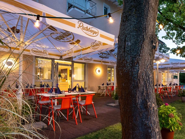 Außengastronomie im Kristallhotel FETTEHENNE Außengastronomie des Kristallhotels FETTEHENNE in Leverkusen mit beleuchteten Tischen unter Bäumen.