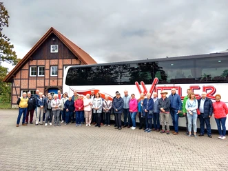 FStadtrundfahrtStadtführerVHS_.jpg Eine Gruppe Touristen steht vor einem großen Reisebus und einem traditionellen Fachwerkhaus.