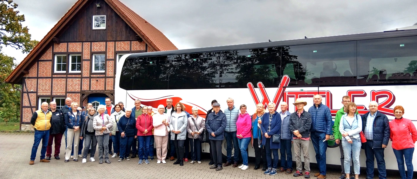 FStadtrundfahrtStadtführerVHS_.jpg Eine Gruppe Touristen steht vor einem großen Reisebus und einem traditionellen Fachwerkhaus.
