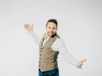 DJ Hendrik Treuse-31.jpg DJ Hendrik Treuse steht mit ausgebreiteten Armen lächelnd vor einem neutralen, hellen Hintergrund.