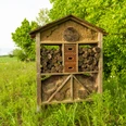 Alte Scheune Historische Dorfschmiede FotoChristianSchwier-070 (8).jpg Ein Insektenhotel aus Holz und Lehm vor einem grünen Feld und Bäumen bei leicht bewölktem Himmel.
