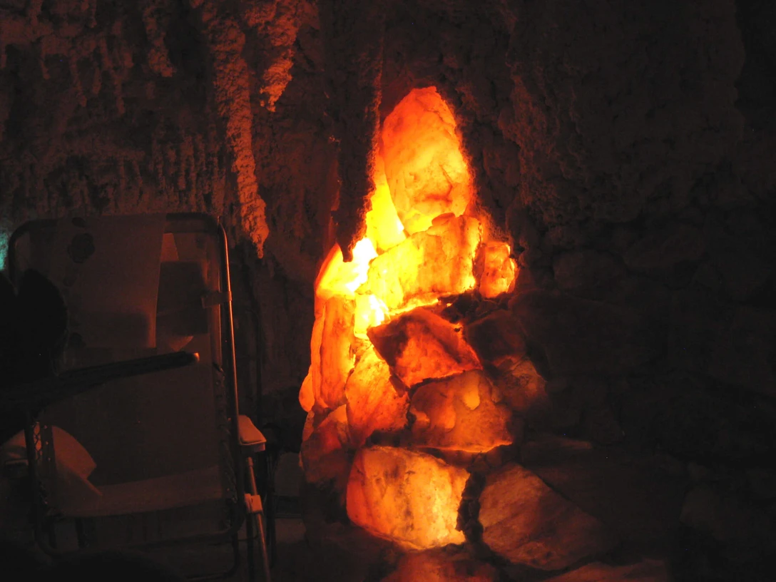 salgrotte-revital-bad-zwischenahn1.jpg Ein stimmungsvoll beleuchteter Raum mit einer Salzkristallformation und Liegen im Dunkeln.