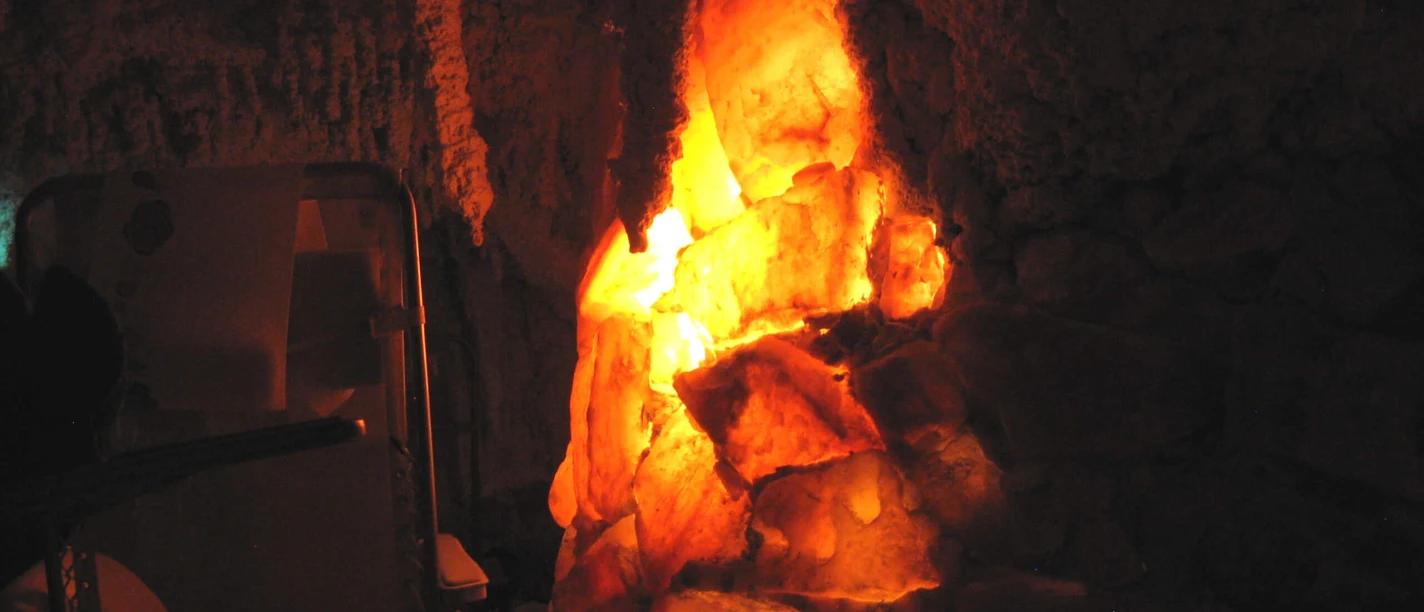 salgrotte-revital-bad-zwischenahn1.jpg Ein stimmungsvoll beleuchteter Raum mit einer Salzkristallformation und Liegen im Dunkeln.