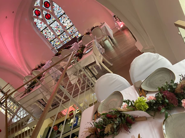 IMG_0970 2.jpeg Tables laid with floral decorations in the gallery of the event chapel with a large stained glass window in the background