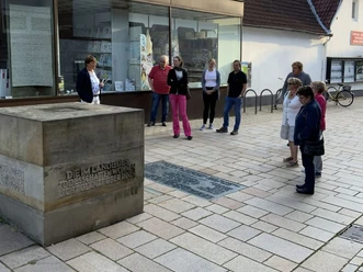 Eine Besuchergruppe hört einem Stadtführer vor einem modernen Gebäude in Lübbecke aufmerksam zu.
