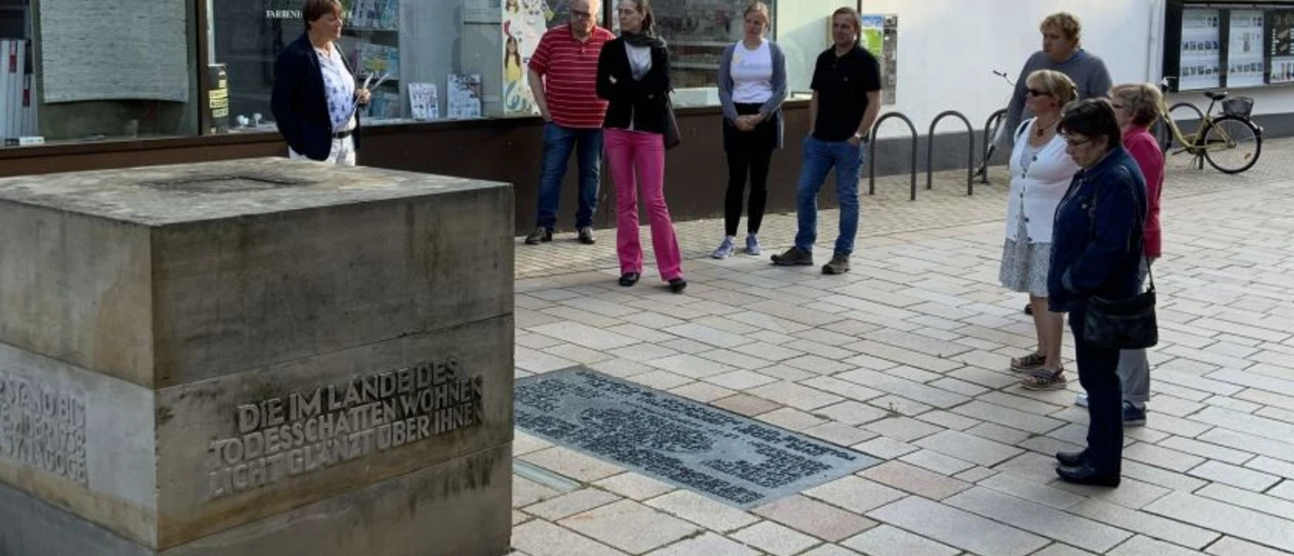 Eine Besuchergruppe hört einem Stadtführer vor einem modernen Gebäude in Lübbecke aufmerksam zu.