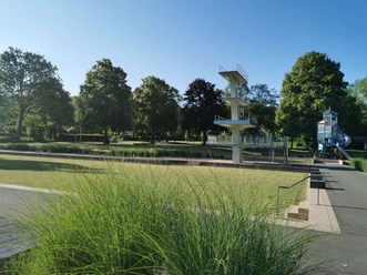 Grünes Freibad mit Sprungturm im Hintergrund, umgeben von schattenspendenden Bäumen und Rasenflächen.